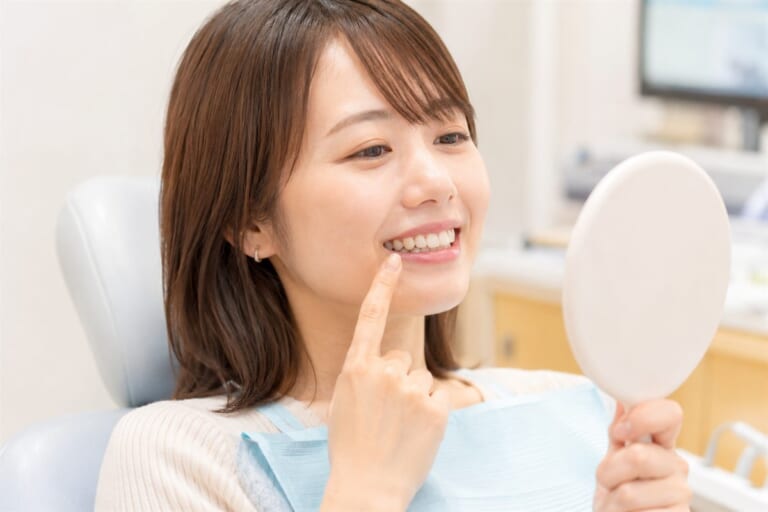 歯科医院のチェアで手鏡を見ながら白くなった歯を確認して笑顔の女性