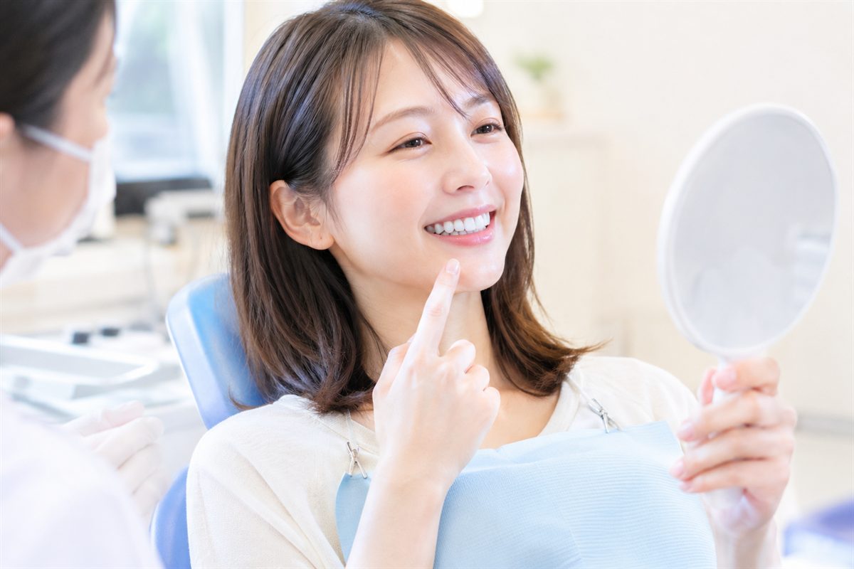 歯科医院で手鏡を持ち、歯科スタッフと一緒に歯の色を確認する女性
